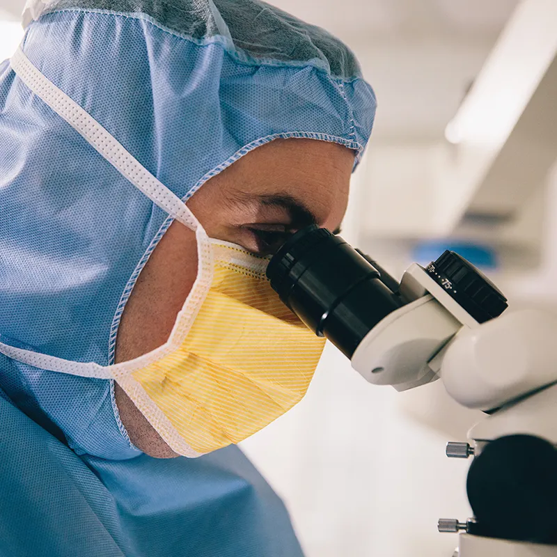 Doctor in medical uniform looking through a microscope
